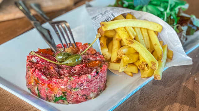 Steak tartare de boeuf finement haché, accompagné de frites croustillantes et d'une petite salade de légumes frais.