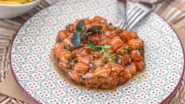 Plat de tartare de saumon finement découpé, mélangé avec des herbes et épices, rehaussé d'une vinaigrette légère à base d'huile d'olive et d'agrumes, garni de jeunes pousses.
