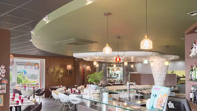 Intérieur de restaurant moderne avec un plafond courbé vert, un bar élégant, un mélange de chaises et tables stylées, un éclairage doux et des éléments décoratifs contemporains.