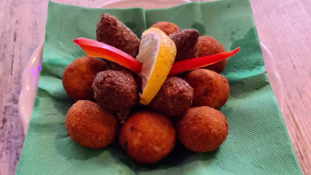 Crocchette dorate di patate e spezie, accompagnate da bocconcini fritti di carne o lenticchie, servite con limone e peperoni rossi.