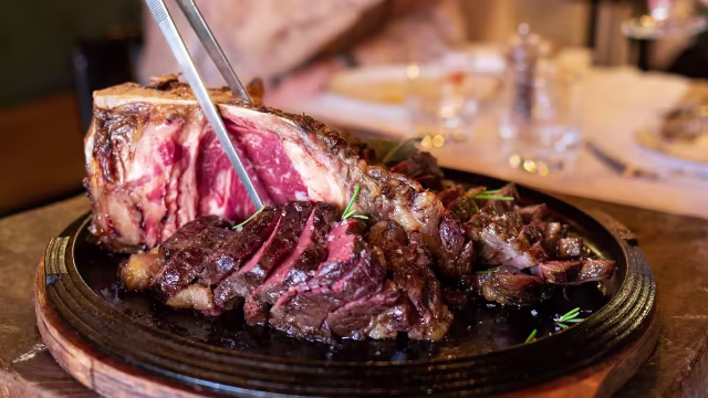 Arrosto di prime rib cotto alla perfezione, con una crosta caramellata e un interno tenero e succoso, servito con rosmarino fresco.