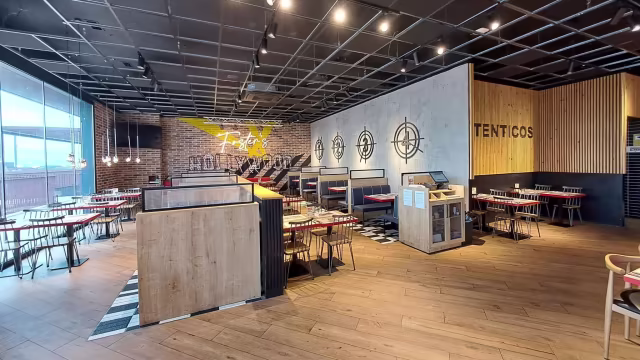 Interior moderno con elementos industriales y acogedores, paredes de ladrillo expuesto y paneles de madera, asientos en elegantes cabinas negras y mesas de madera, iluminación suave y arte mural con motivos de diana.