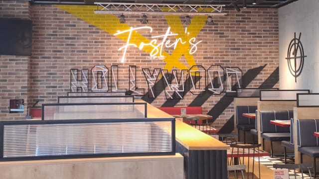 Interior moderno de restaurante con diseño de ladrillo, elementos gráficos en negro y amarillo, y nombre iluminado en neón. Dispone de cómodos asientos en cabinas y sillas elegantes, ideal para la interacción social.