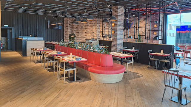 Interior moderno con elementos de madera e industrial, bancos curvos rojos, paredes de ladrillo expuesto y iluminación ambiental, creando un ambiente acogedor.