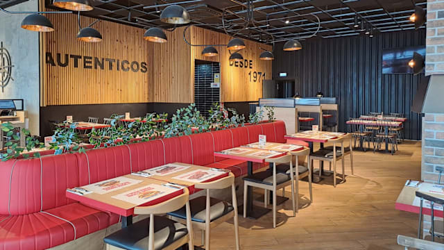 Interior moderno con paneles de madera, asientos cómodos en tonos rojos, mesas de madera y una iluminación elegante, creando un ambiente acogedor y contemporáneo.