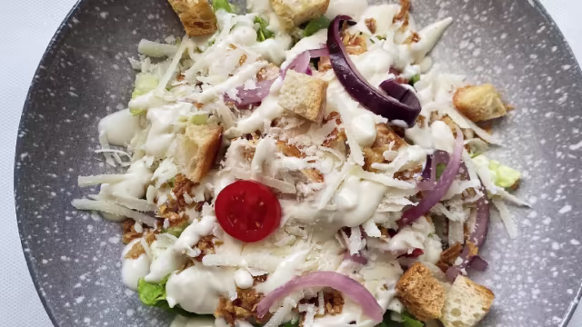 Ensalada fresca de lechuga crujiente, con queso rallado, picatostes, cebolla roja y tomate cherry, aderezada con una crema suave.