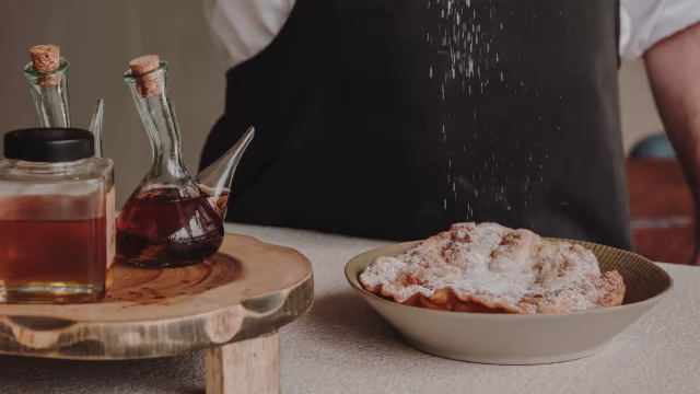 Pasteles recién hechos, dorados y crujientes, espolvoreados con azúcar glas, acompañados de jarabes oscuros.