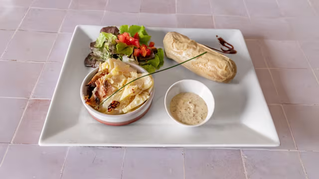 Plat de casserole crémeuse avec une croûte dorée, accompagné d'un mélange de salades et d'un petit pain grillé.