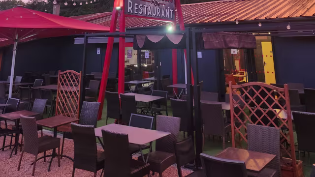 Espace de restauration en plein air avec des tables en bois et des chaises en osier, agrémenté d'un auvent rouge et de panneaux décoratifs, créant une ambiance chaleureuse et accueillante.