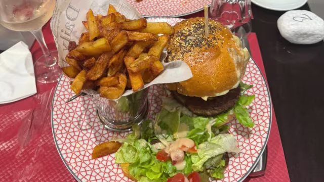 Burger copieux dans un pain au sésame, garni de mayonnaise crémeuse et accompagné d'une salade fraîche et de frites épaisses et croustillantes.