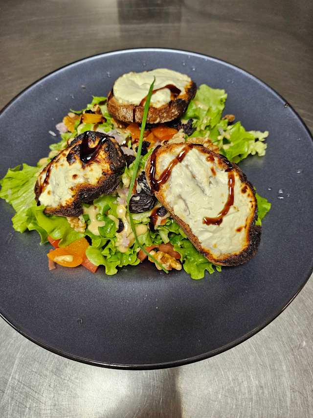 Salade fraîche de légumes à feuilles avec tomates en dés et herbes hachées, accompagnée de pain grillé et d'un filet de réduction balsamique.