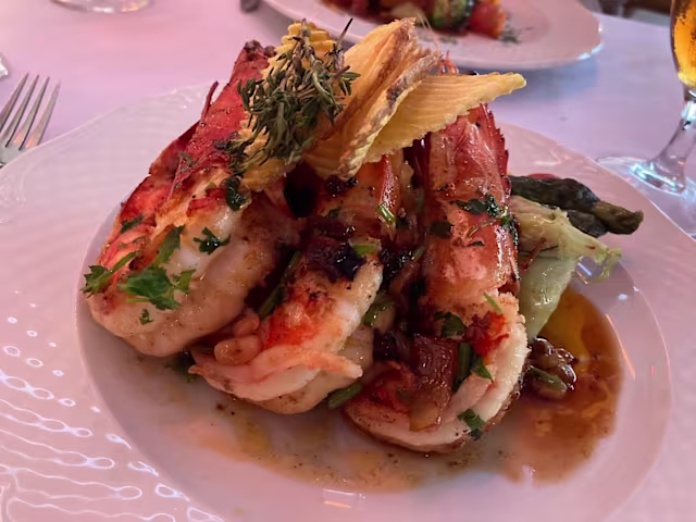 Prato elegantemente apresentado com grandes camarões suculentos grelhados, guarnecidos com ervas frescas, acompanhados de espargos tenros e uma mistura de legumes salteados, regados com um molho saboroso.