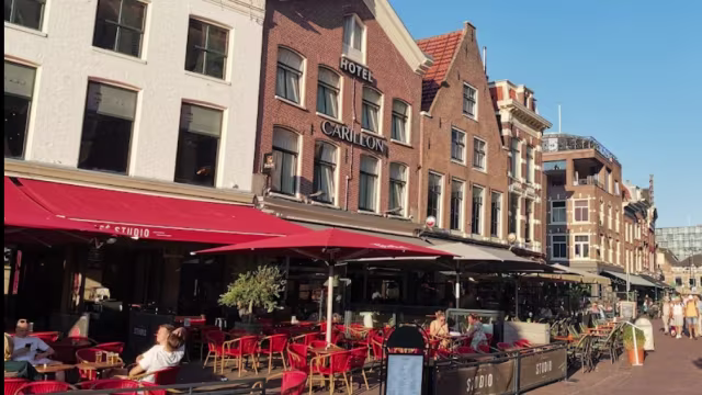 Charmante restaurantgevel met een mix van bakstenen en witte facades, voorzien van buitenzitplaatsen met rode stoelen en tafels, omgeven door grote parasols voor schaduw.