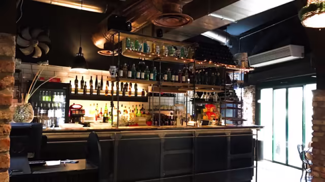 Interno di un bar moderno con design industriale, caratterizzato da un bancone elegante, pareti in mattoni a vista e illuminazione calda.