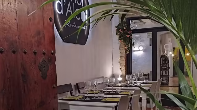 Interior de restaurante acogedor con elementos de madera, mesas con manteles blancos y cristalería elegante, creando un ambiente cálido y sofisticado.