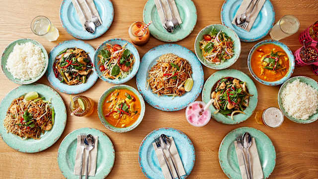 A vibrant selection of Asian-inspired dishes including a creamy orange curry garnished with fresh herbs and lime, stir-fried noodles with vegetables, and bowls of rice for a communal dining experience.