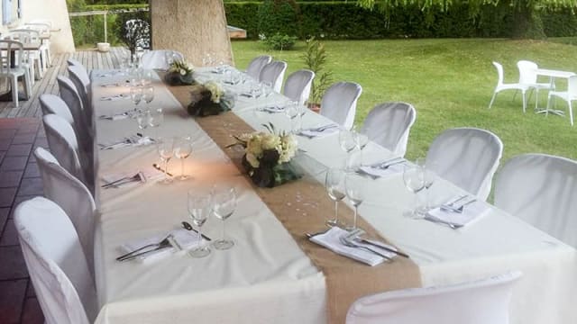 Table élégamment dressée en extérieur, avec des nappes blanches, des chaises blanches et des arrangements floraux, créant une atmosphère accueillante pour des occasions spéciales.