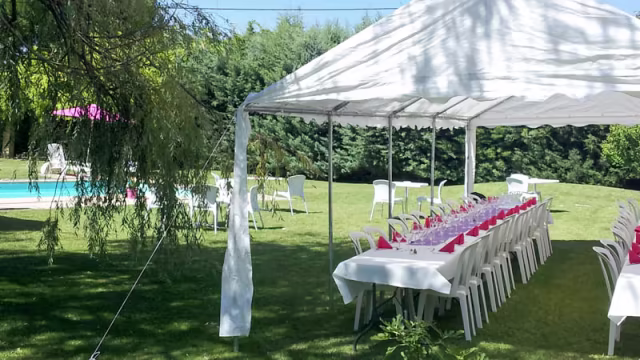 Installation de restauration en plein air sous un chapiteau blanc, avec une table élégamment dressée, entourée de verdure et d'une piscine bleue en arrière-plan, idéale pour des rassemblements festifs.