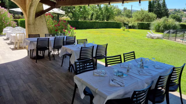 Espace de restauration en plein air avec des tables sur un patio, entouré de verdure luxuriante et de plantes fleuries, créant une ambiance sereine et accueillante.