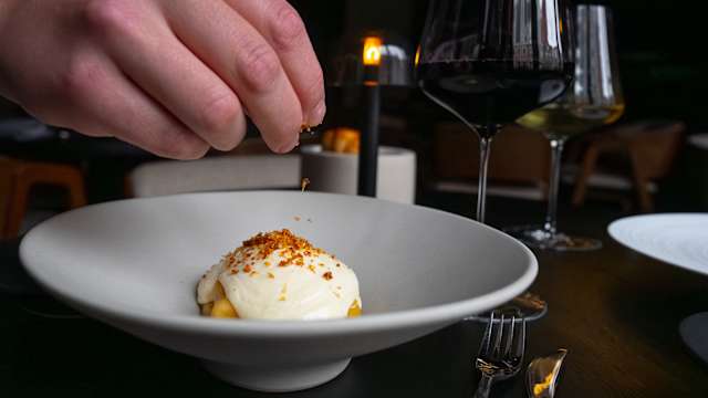 Een verfijnd dessert met een romige laag, gegarneerd met een sprenkel knapperige kruimels van noten of koekjes, wat de visuele aantrekkingskracht versterkt.