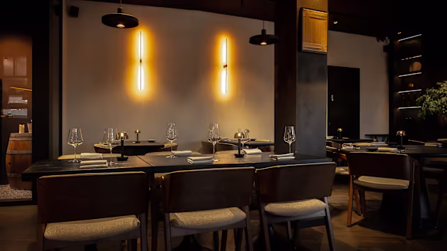 Modern restaurantinterieur met donkere houten tafels en stoelen, minimalistisch ingericht met enkele decoratieve elementen zoals potplanten en sfeervolle verlichting voor een intieme sfeer.