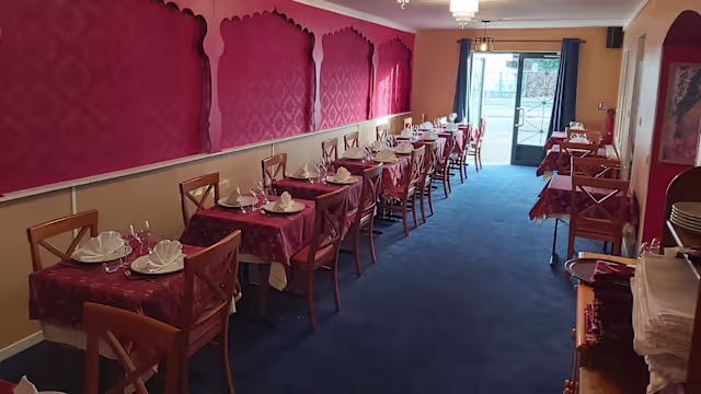 Intérieur de restaurant chaleureux avec des tables soigneusement dressées, nappées de rouge, et décorations murales élaborées, créant une ambiance accueillante.