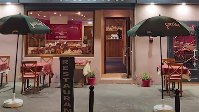 Extérieur d'un restaurant accueillant avec une ambiance chaleureuse, comprenant des tables en plein air ornées de nappes à carreaux rouges et des parasols verts, créant une atmosphère décontractée.