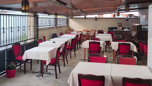 Espace de restauration en plein air avec des tables sous un auvent en bois, nappées de couleurs claires et entourées de chaises en tissu rouge, créant une atmosphère chaleureuse et accueillante.
