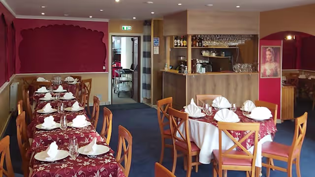 Intérieur de restaurant chaleureux avec des tables bien dressées, nappes blanches et murs rouges, créant une ambiance accueillante.