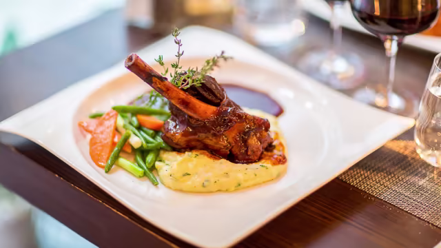 "Vackert presenterad lammlägg med en rik sås, serverad med krämig polenta, stekta gröna bönor och färgglada morötter, garnerad med timjan."