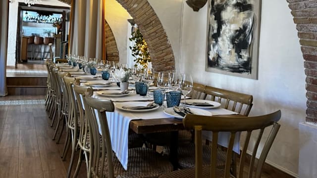Área de comedor amplia con mesas de madera, manteles blancos y decoración elegante, destacando paredes de piedra arqueadas y acentos de madera cálidos.