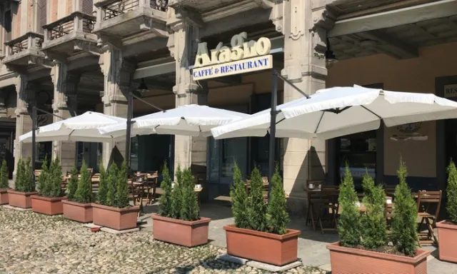 Esterno del ristorante "Akasro" con tavoli all'aperto sotto ombrelloni bianchi, circondato da piante verdi e dettagli architettonici classici.