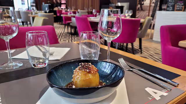 Plat rond doré, probablement un gâteau salé ou un dumpling, servi sur une sauce sombre et brillante, garni de graines de sésame pour une touche croquante et savoureuse.