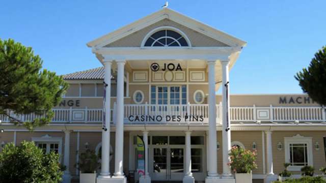Extérieur du restaurant "Casino des Pins" avec une entrée majestueuse, des colonnes blanches et une grande fenêtre en arc, entouré de verdure soigneusement entretenue.