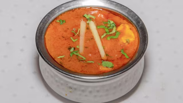 Curry aromático con salsa a base de tomate, trozos de pollo o paneer, decorado con hierbas frescas y jengibre.