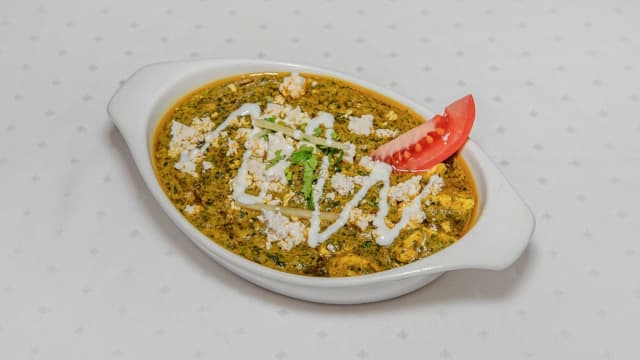 Plato cremoso con salsa verde de espinacas, cubierto de queso blanco desmenuzado, yogur y rodaja de tomate fresco.