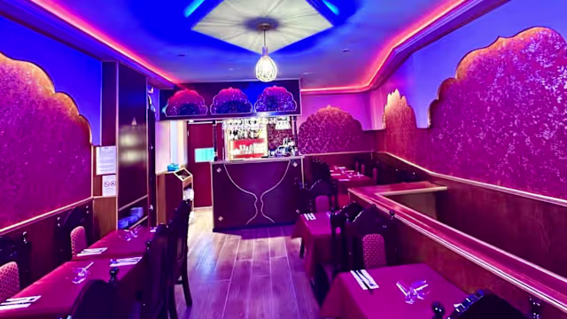 Intérieur du restaurant chaleureux avec des murs rouges ornés de motifs, éclairage doux et ambiance cosy, sièges en bois foncé avec rembourrage rouge, et éléments décoratifs élégants.