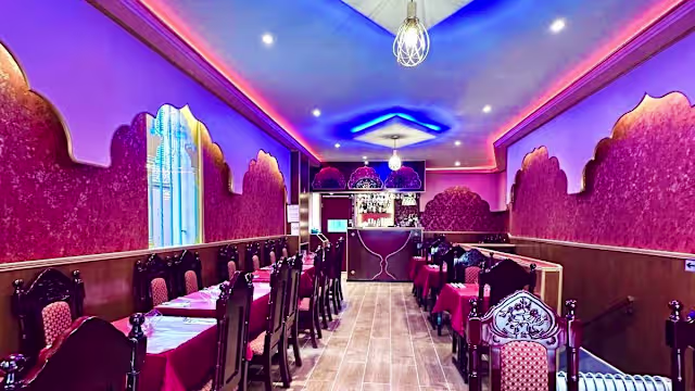 Intérieur du restaurant chaleureux avec des murs rouges ornés, chaises en bois foncé et éclairage doux, créant une ambiance accueillante.