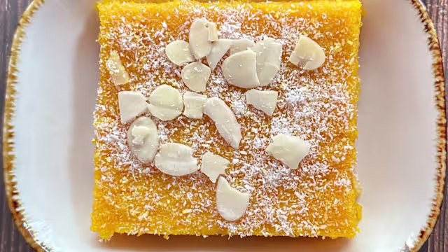 Gâteau carré à base de semoule ou de maïs, garni de noix de coco râpée et d'amandes effilées, offrant une texture croquante et une légère mâche.