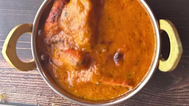 Plat crémeux de morceaux de viande tendre, probablement de poulet, dans une sauce épaisse de couleur orange à base de tomates et d'épices, agrémenté de petites herbes vertes.