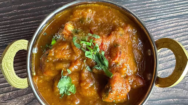 Plat aromatique de morceaux de viande tendre, probablement de poulet, mijotés dans une épaisse sauce épicée de couleur rougeâtre, garni de coriandre fraîche.