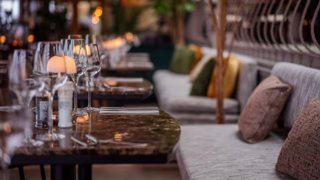 Stijlvol restaurantinterieur met elegant gedekte tafels, pluche banken in gedempte tinten en een uitnodigende, verfijnde sfeer.