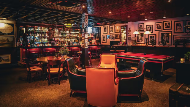 Gezellige restaurantinterieur met een bar, warme verlichting, comfortabele stoelen, kunst aan de muren en een pooltafel, ideaal voor een ontspannen sfeer.