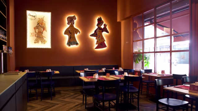 Interno di un ristorante moderno con tonalità calde e terrose, sedie e tavoli in legno scuro, e un'accogliente zona booth. Atmosfera invitante e ben progettata per un'esperienza di ristorazione informale.