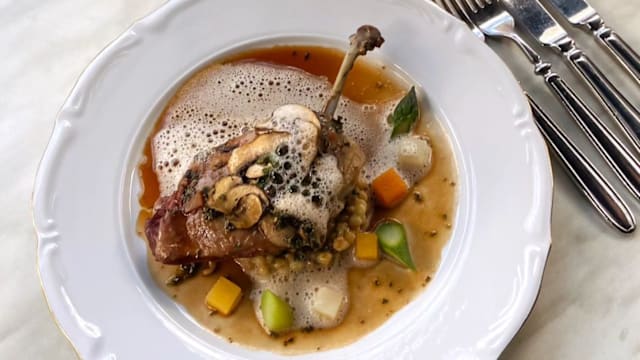 Gerecht met malse eend op een bed van romige granen, gegarneerd met gesneden champignons en kruiden, omringd door een rijke bouillon met een delicate schuimlaag en kleurrijke groentecubes.