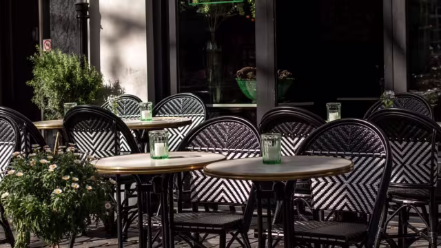 Buiten eetgedeelte met ronde tafels en zwart-wit gestreepte stoelen, versierd met groene glazen en omringd door potplanten met witte bloemen, ideaal voor casual dineren of een drankje in de open lucht.