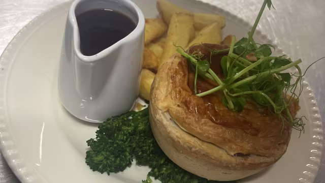 Golden-brown meat pie with a flaky crust, served with crispy chips, steamed broccoli, and a side of dark gravy.