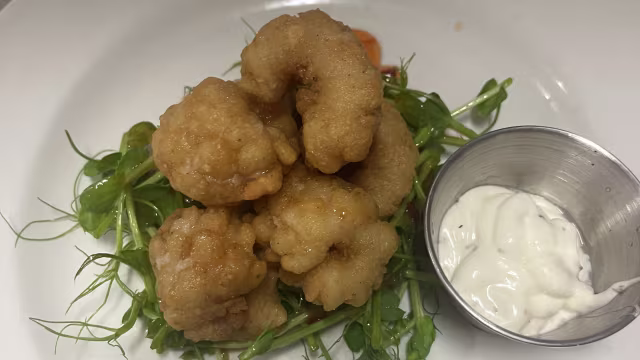 Crispy golden-brown fried shrimp served on a bed of fresh microgreens, accompanied by a creamy dipping sauce.
