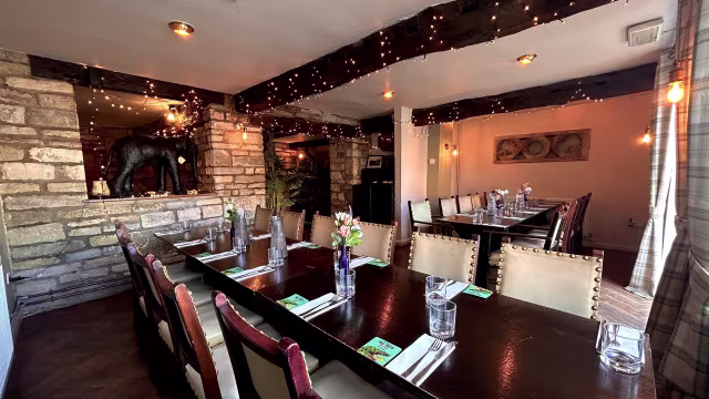 Cozy restaurant interior with rustic wooden beams, stone walls, soft lighting, and decorative plants, designed for communal dining.