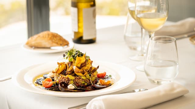 Quinoa en capas con chips de verduras crujientes, tomates cherry y salsa cremosa, decorada con microgreens.